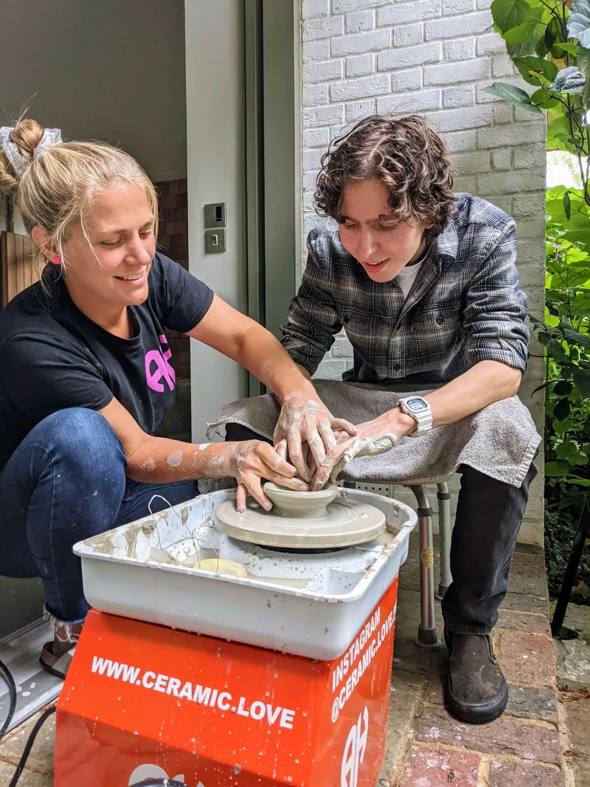 Amanda helping a student shape clay on the pottery wheel