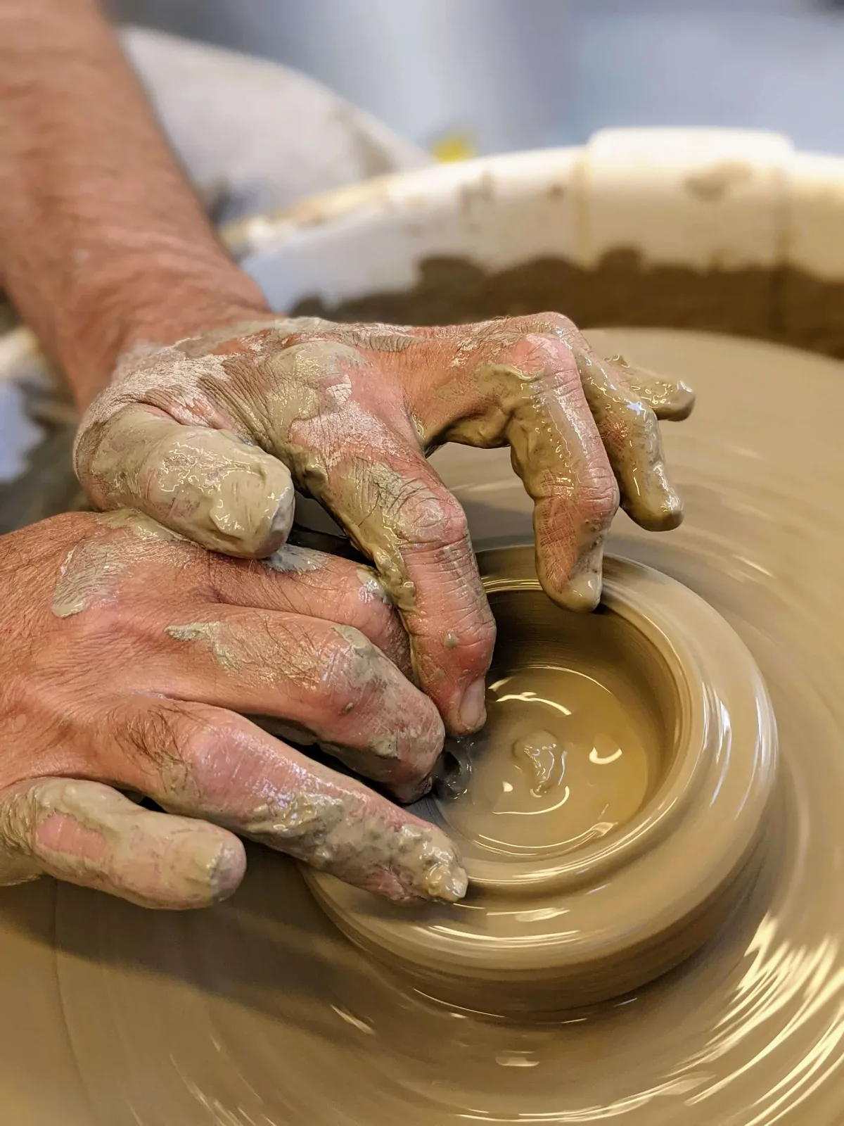 Clay-covered hands shaping a pot on the wheel