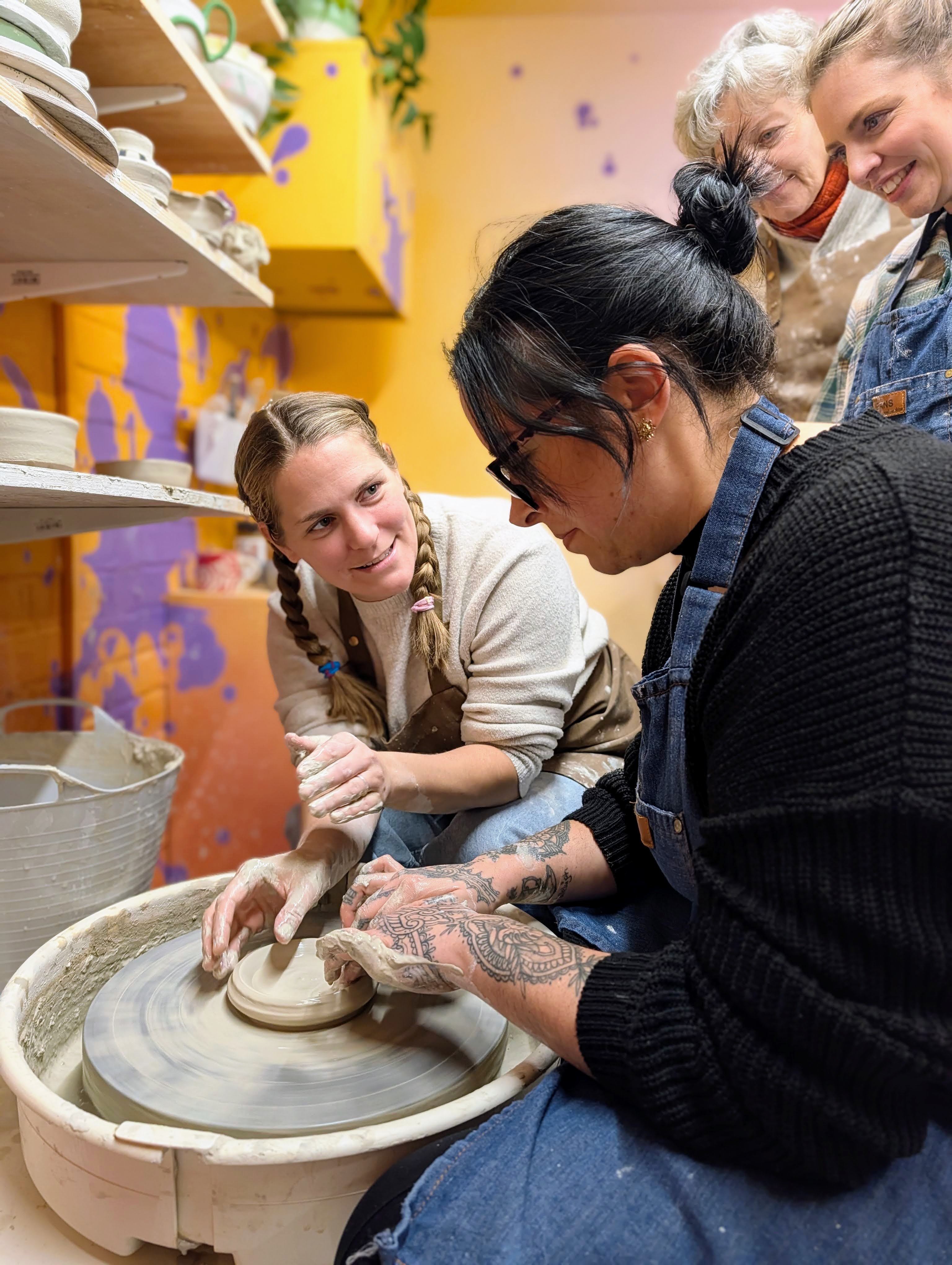 Amanda guiding a student at the pottery wheel during a class at Ceramic Love studio